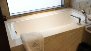A modern bathroom with a large bathtub, a towel, and a trash bin. - Longtan Lake Hotel (Shangrao)