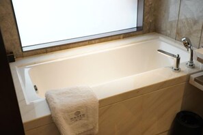 A modern bathroom with a large bathtub, a towel, and a trash bin. - Longtan Lake Hotel (Shangrao)