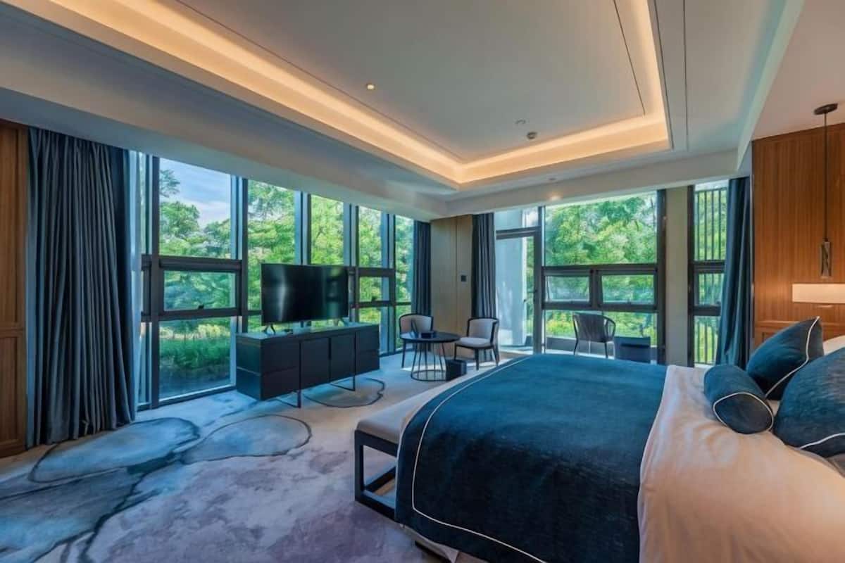Une chambre moderne dotée d’un grand lit, d’une télévision, d’un coin salon et de grandes fenêtres.