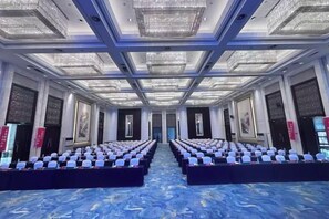 Un salón de conferencias con filas de sillas, alfombra azul y candelabros.