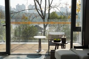 A balcony with a glass door, a round table, a sofa, and a view of trees and buildings. - Longtan Lake Hotel (Shangrao)