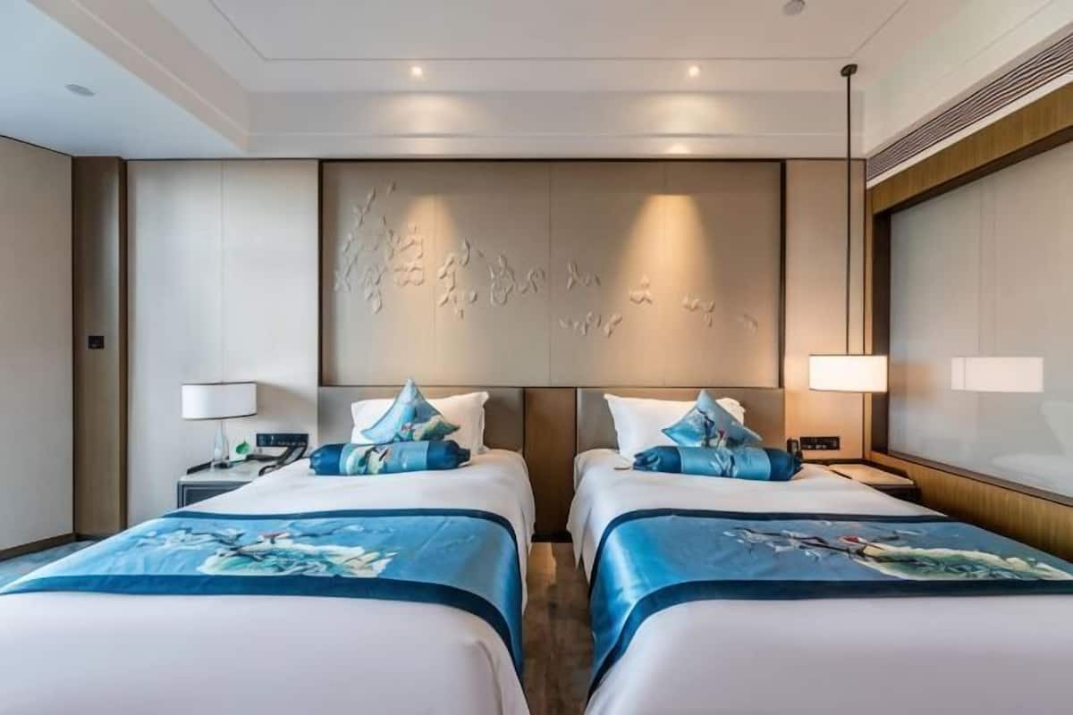 Une chambre d’hôtel avec deux lits, une grande œuvre d’art accrochée au mur et une fenêtre donnant sur un beau paysage.
