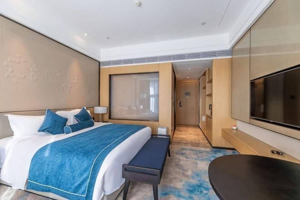 Une chambre d’hôtel avec un lit, un banc, une télévision et une grande fenêtre.