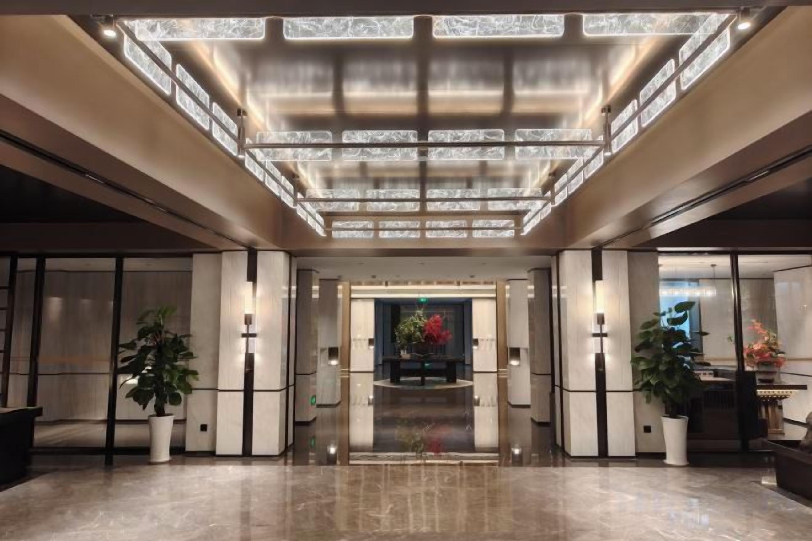 A spacious lobby with a high ceiling, a central floral arrangement, and potted plants.
