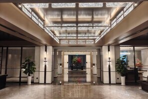 A spacious lobby with a high ceiling, a central floral arrangement, and potted plants. - Longtan Lake Hotel (Shangrao)