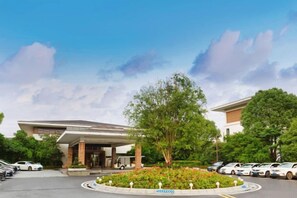 A hotel entrance with a covered parking area, a landscaped garden, and a clear sky. - Longtan Lake Hotel (Shangrao)