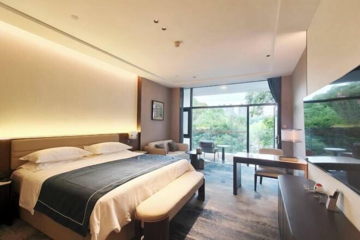 Une chambre dâhĂŽtel moderne, dotĂ©e dâun grand lit, dâun bureau, dâune chaise et offrant une vue sur lâextĂ©rieur.