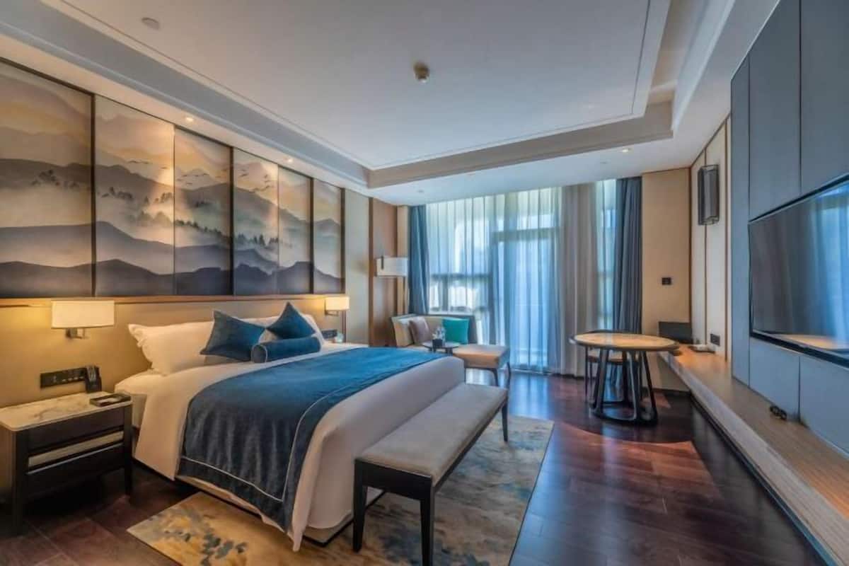 Une chambre d’hôtel moderne dotée d’un grand lit, de tables de chevet, d’un banc, d’une télévision et offrant une vue sur l’extérieur.