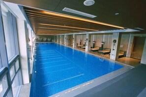 A swimming pool with a clear blue water surface, surrounded by a modern interior with glass walls and wooden ceiling panels. - Longtan Lake Hotel (Shangrao)