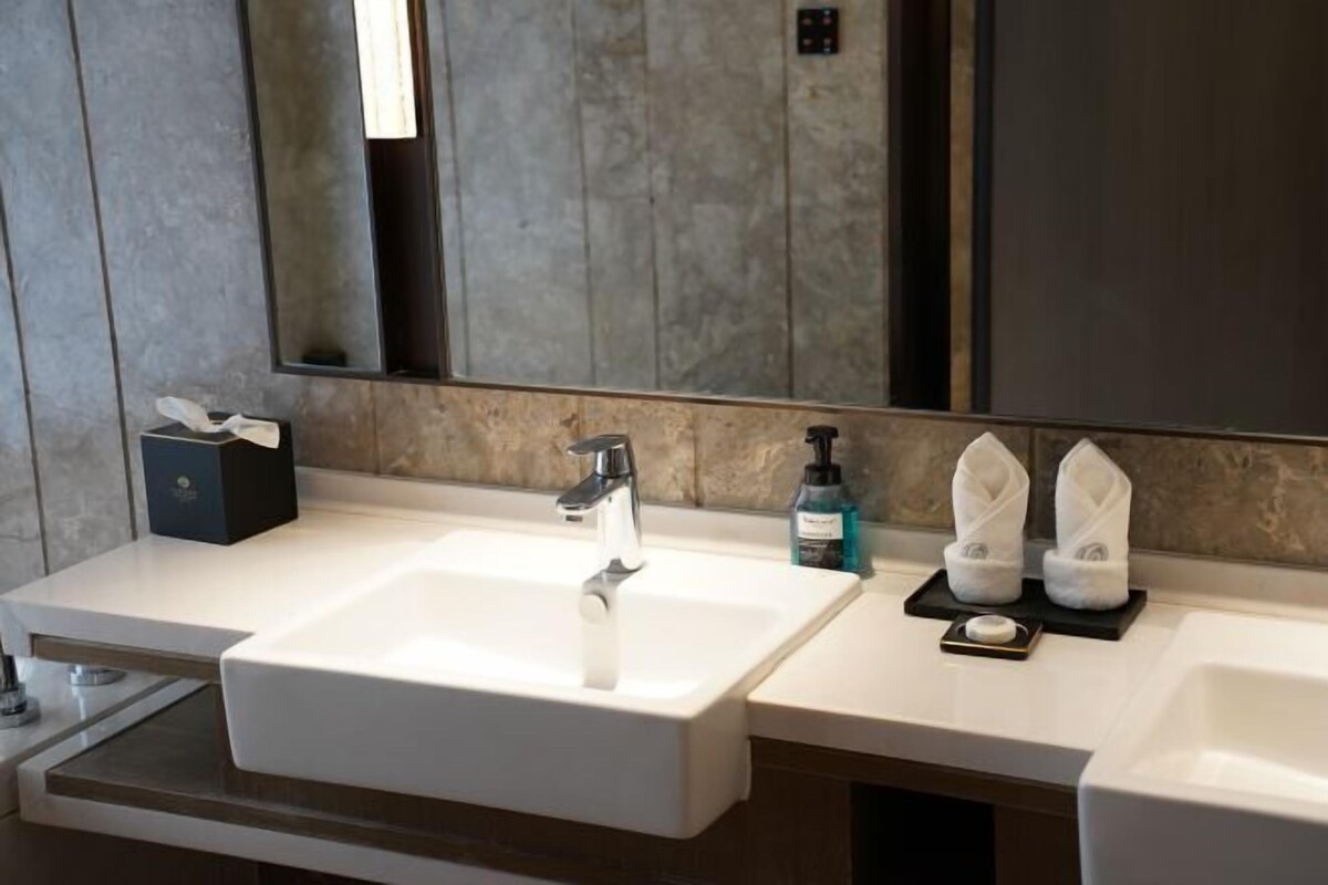 A modern bathroom with a large mirror, a white sink, and a countertop with toiletries.