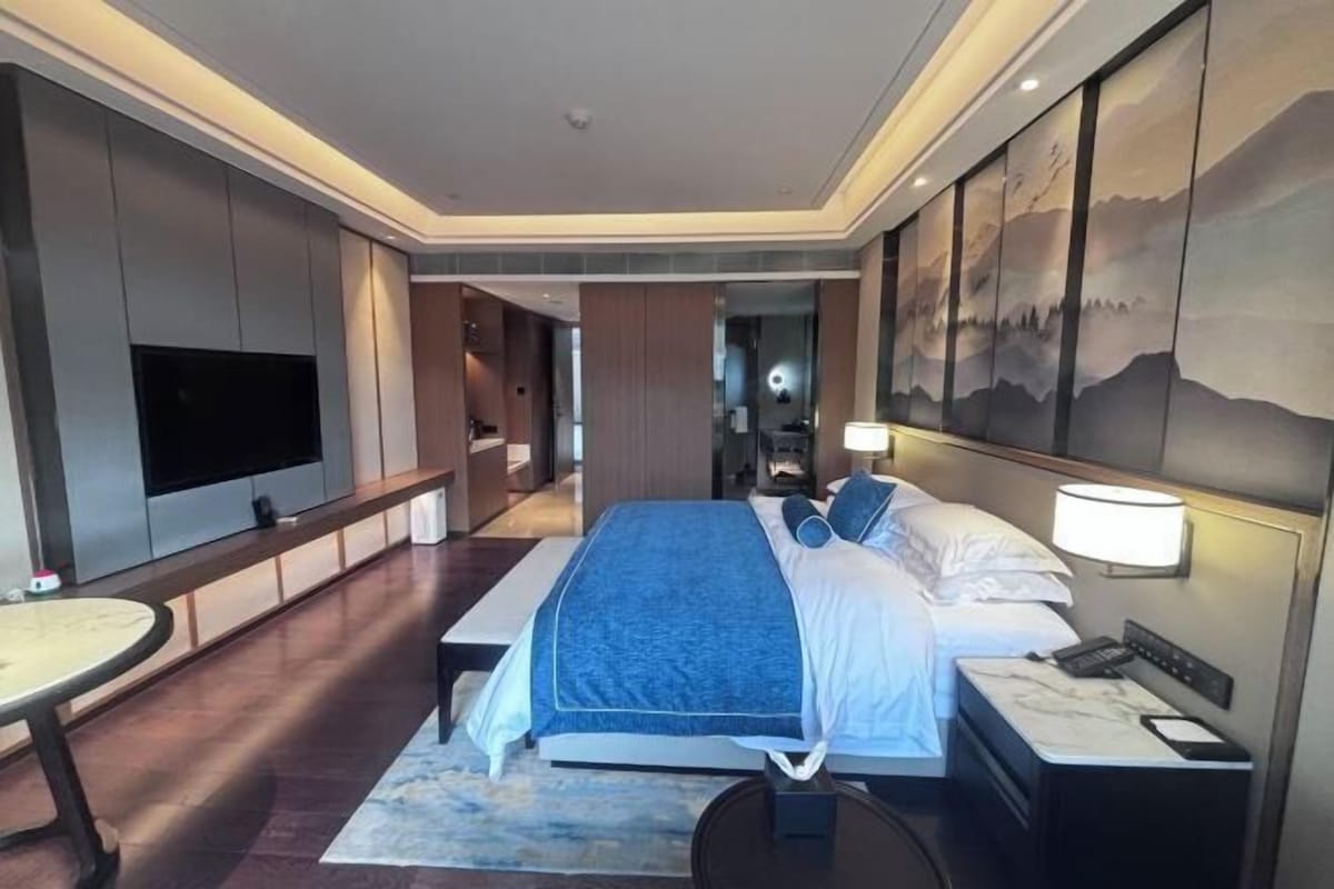 A hotel room with a bed, bedside table, lamp, and a TV mounted on the wall.