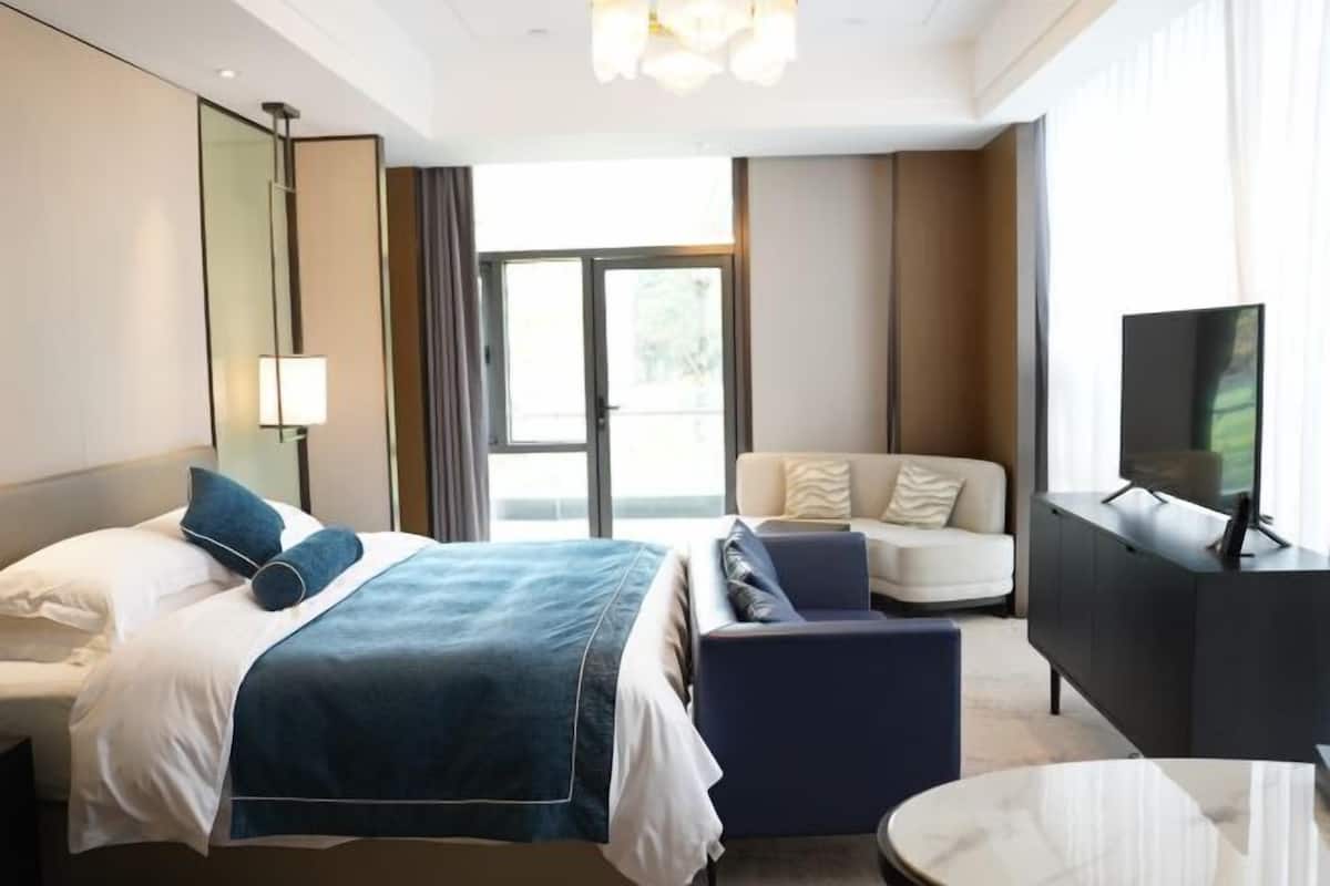 Une chambre d’hôtel avec un lit, un canapé, une télévision et une grande fenêtre.