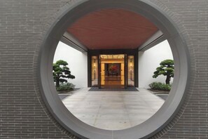 Estructura arquitectónica circular con muro de ladrillo y techo rojo, que conduce a la entrada de un edificio.