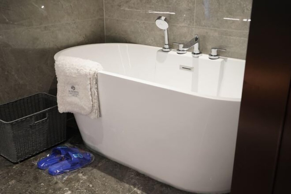 A bathroom with a white bathtub, a towel hanging on the side, and a black basket on the floor.