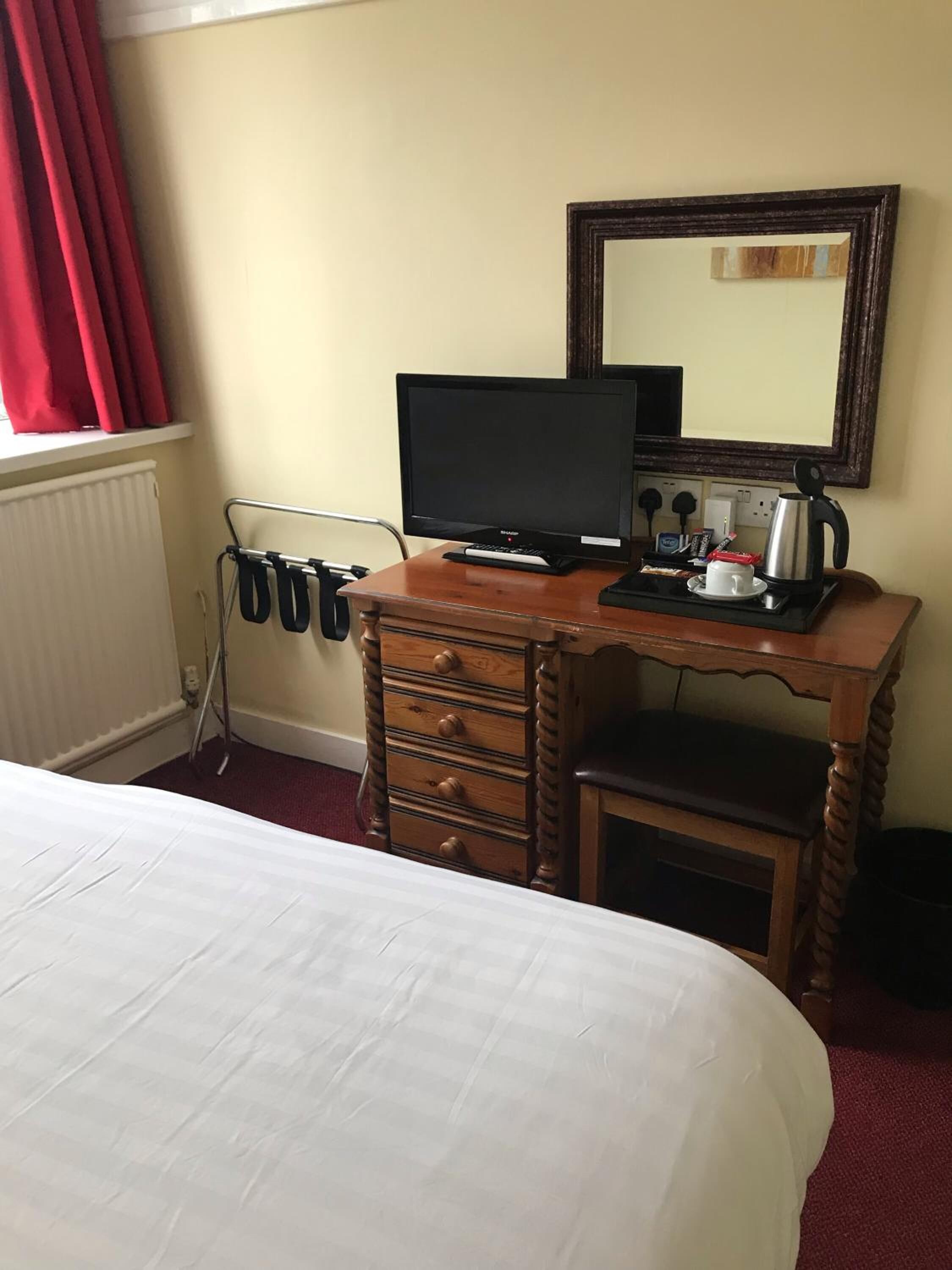 A hotel room with a bed, a desk with a computer, a coffee maker, and a mirror.