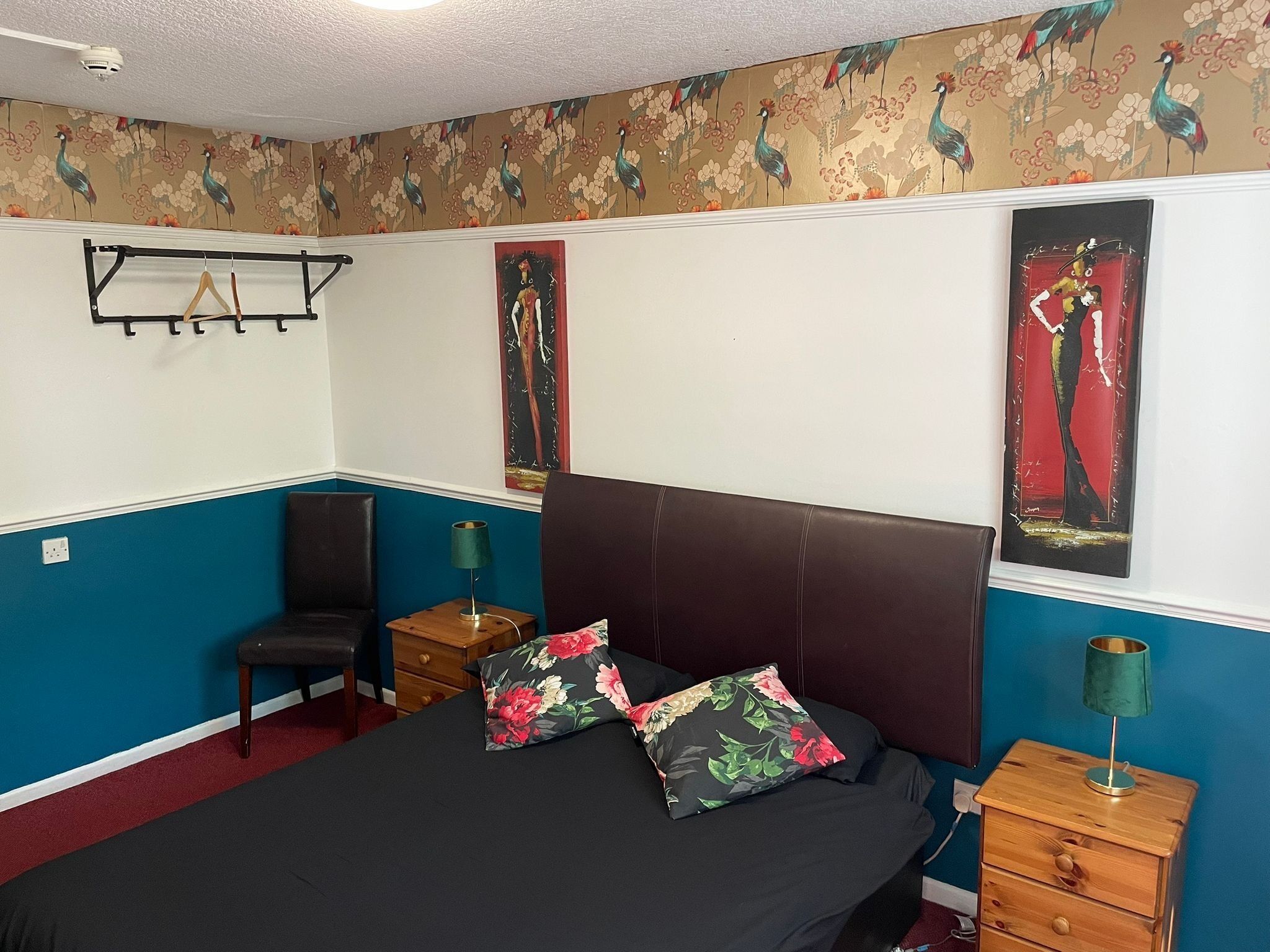 Un dormitorio con cama, una silla, una mesita de noche y un perchero en la pared.