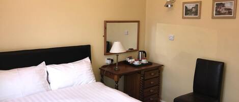 A hotel room with a bed, a wooden dresser, a chair, a lamp, and two framed pictures on the wall.