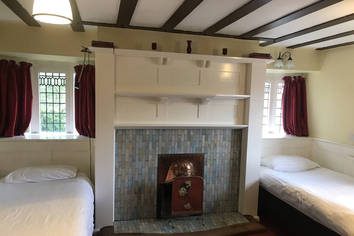 A room with two beds, a fireplace, and a window with curtains.