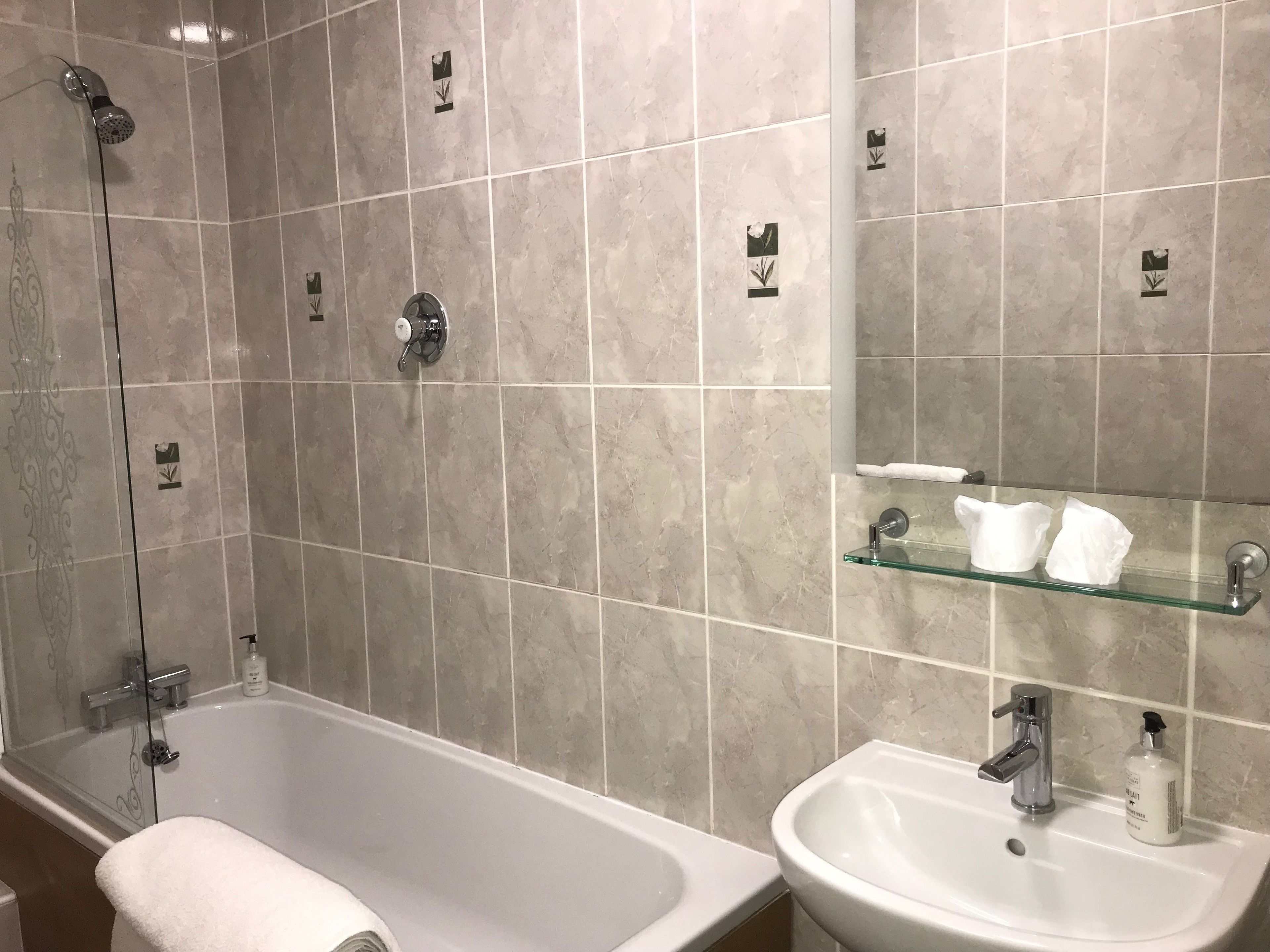 A bathroom with a bathtub, a sink, and a glass shelf with toiletries.