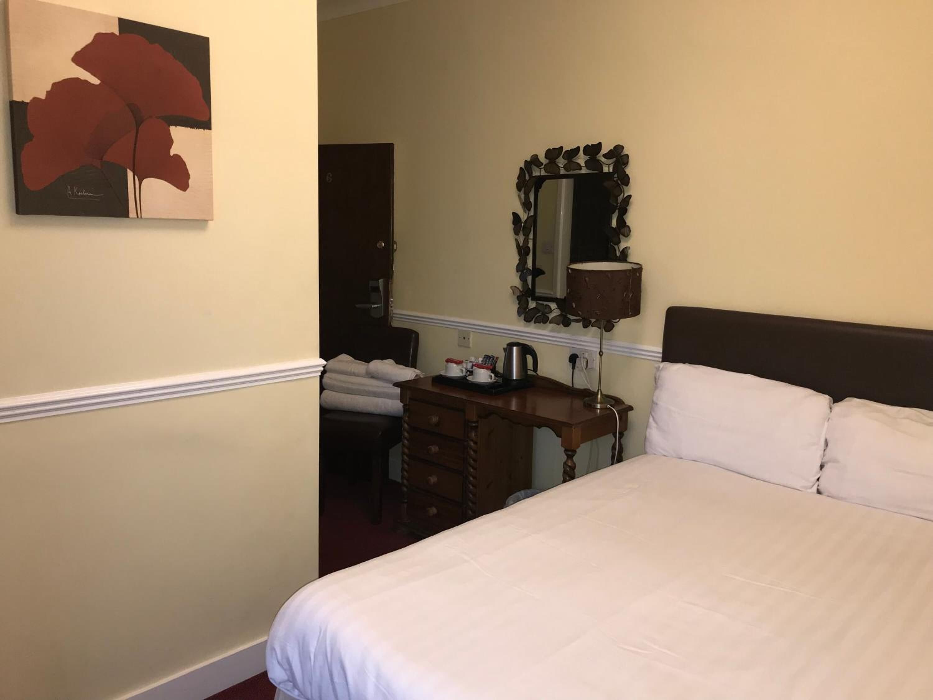 A hotel room with a bed, a desk with a lamp, a mirror, and a painting on the wall.