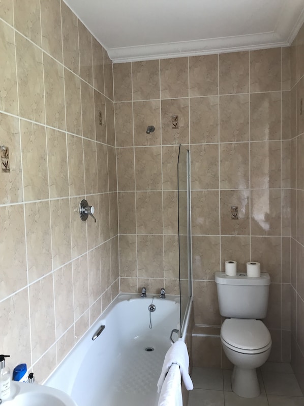 Un baño con baldosas color beige, una bañera, un inodoro y una ducha.