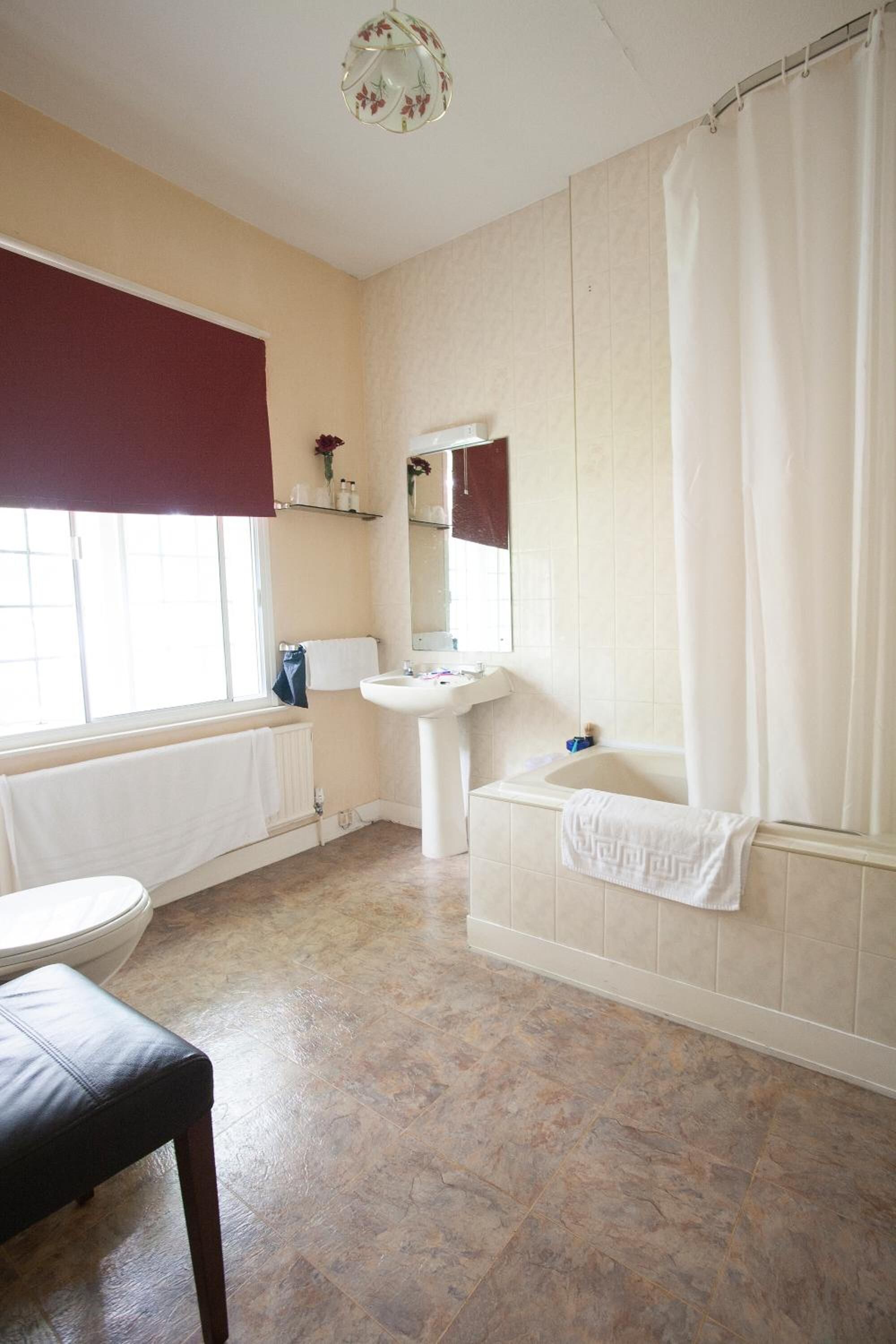 A bathroom with a toilet, sink, bathtub, and a bench.