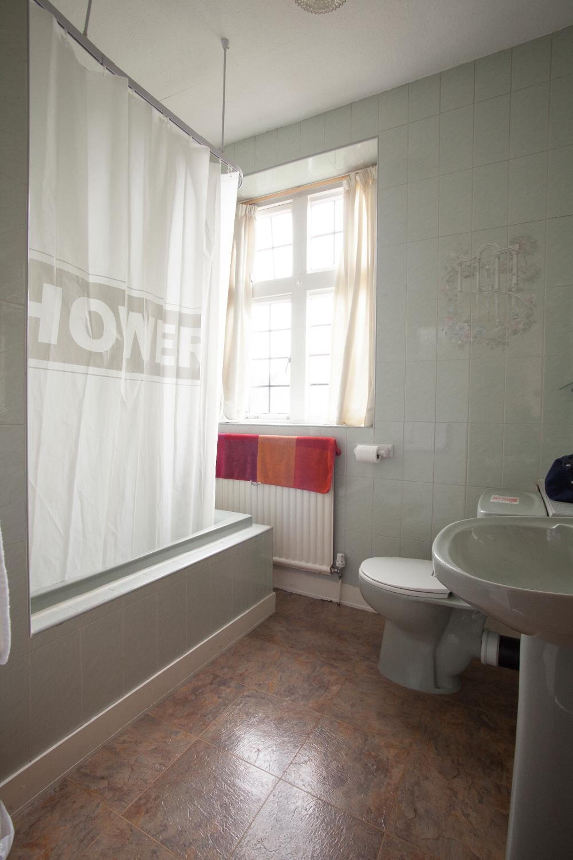 Une salle de bain avec un rideau de douche, une fenêtre avec des rideaux, un radiateur, des toilettes et un lavabo.