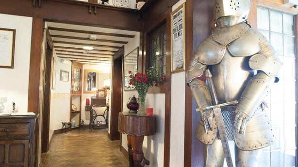 A hallway with wooden beams, a large suit of armor, and a wooden floor. - Barons Court Hotel (Wolverhampton)