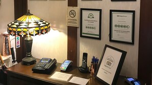 A reception desk with framed certificates of excellence, a telephone, a cash register, and a decorative lamp. - Barons Court Hotel (Wolverhampton)