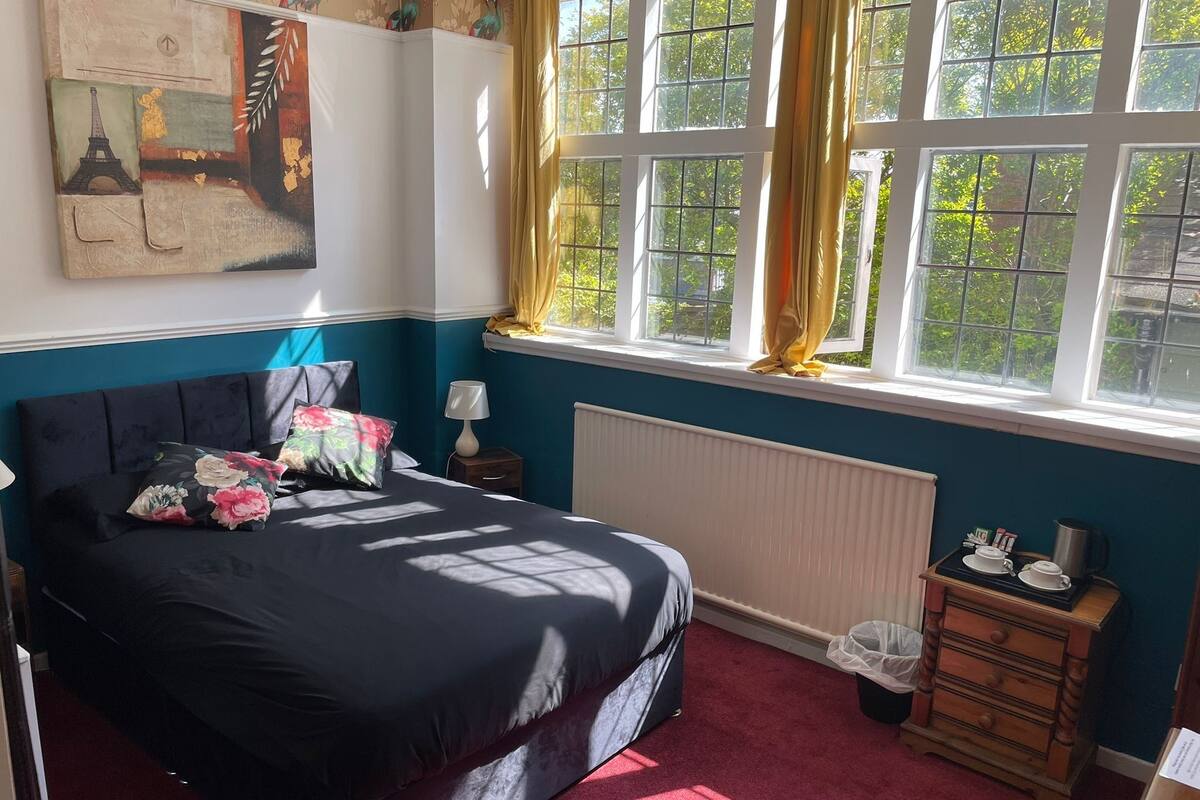 A bedroom with a bed, a nightstand, a dresser, a radiator, and a window with curtains.