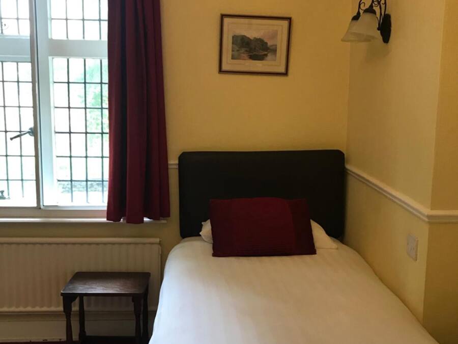 Une pièce comprenant un lit, une fenêtre avec des rideaux, une petite table et un luminaire fixé au mur.