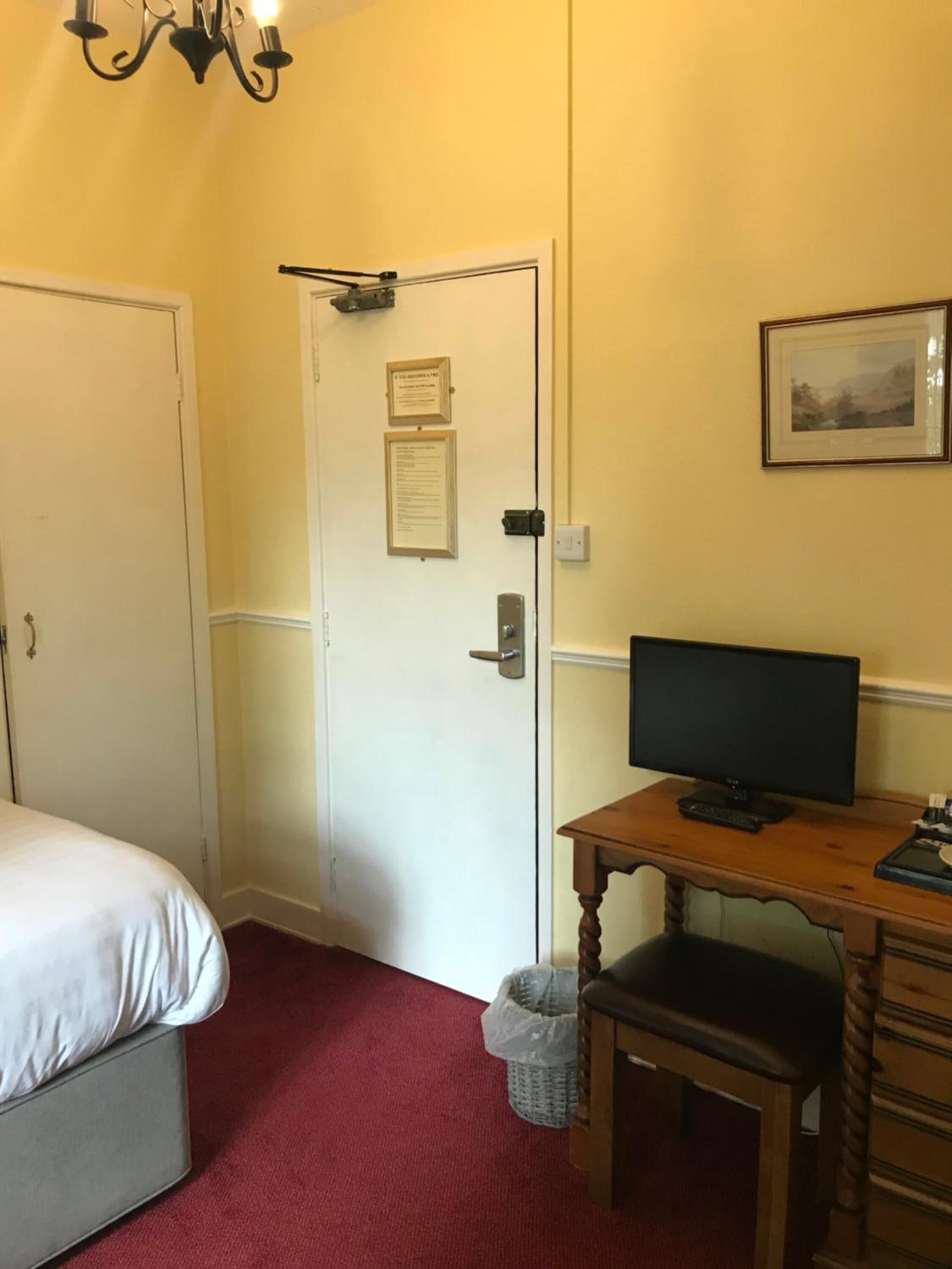 Une chambre d’hôtel avec un lit, un bureau équipé d’un ordinateur, une poubelle et une porte sur laquelle est affiché un avis.