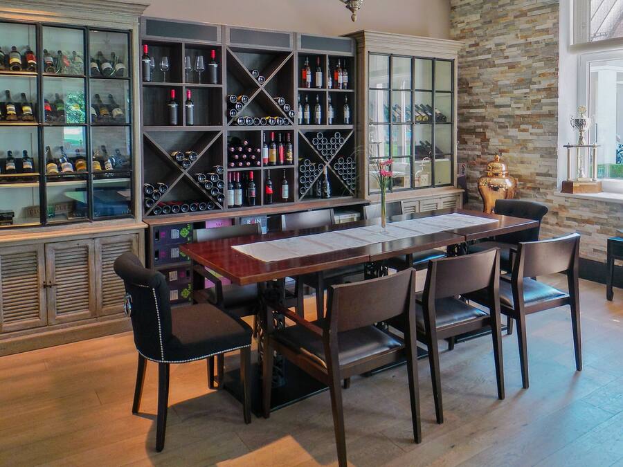 A bar area with a long wooden table and several chairs, surrounded by shelves filled with bottles and glasses.