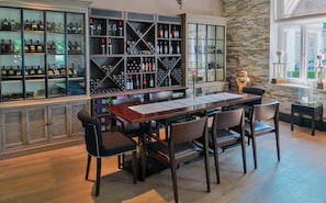 A bar area with a long wooden table and several chairs, surrounded by shelves filled with bottles and glasses. - Hotel Diamond Country Club (Atzenbrugg)
