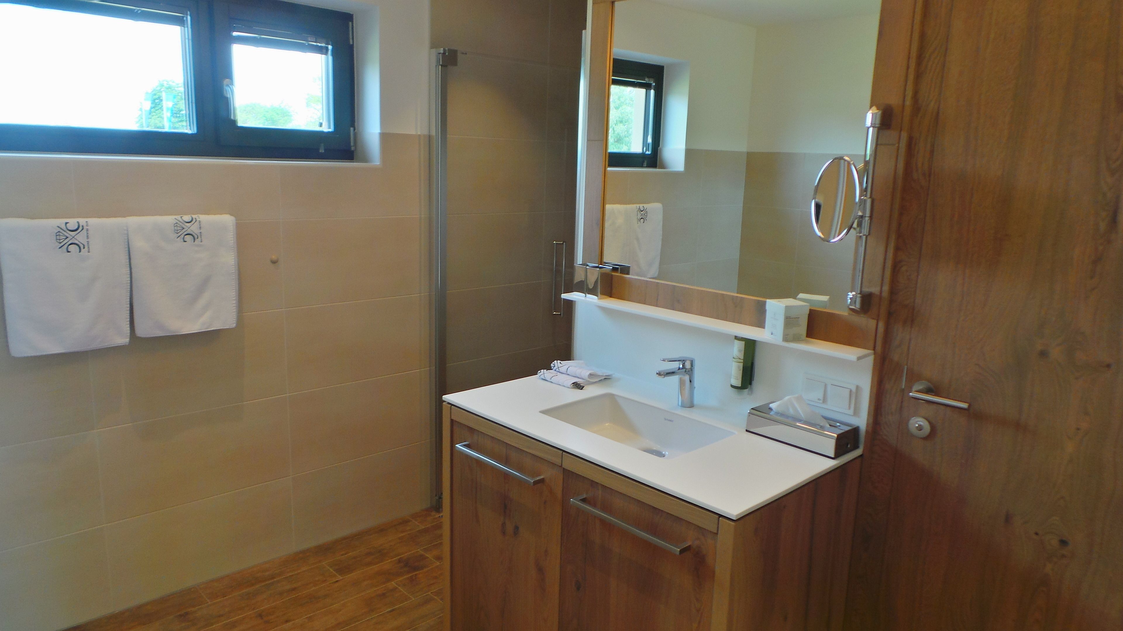 A modern bathroom with a wooden vanity, a large mirror, and a window above the sink.