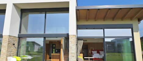 A modern two-story house with large glass doors leading to a dining area and a bedroom.