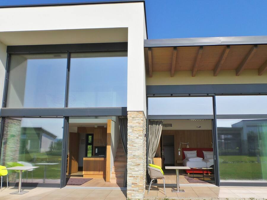 A modern two-story house with large glass doors leading to a dining area and a bedroom.