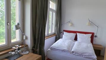 Un dormitorio con una cama, dos mesitas de noche, un escritorio con copas de vino y una ventana con cortinas.