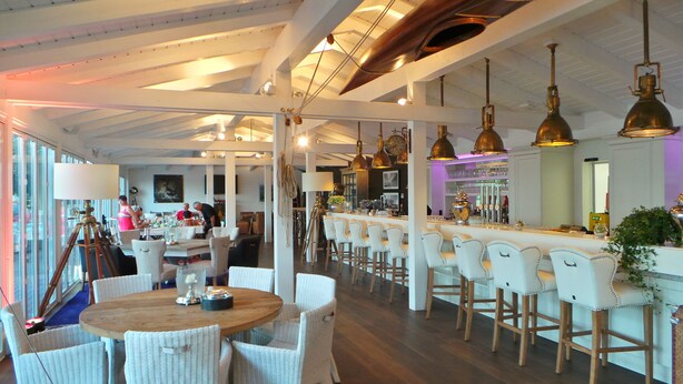A modern bar area with white bar stools, a round wooden table, and pendant lighting. - Hotel Diamond Country Club (Atzenbrugg)