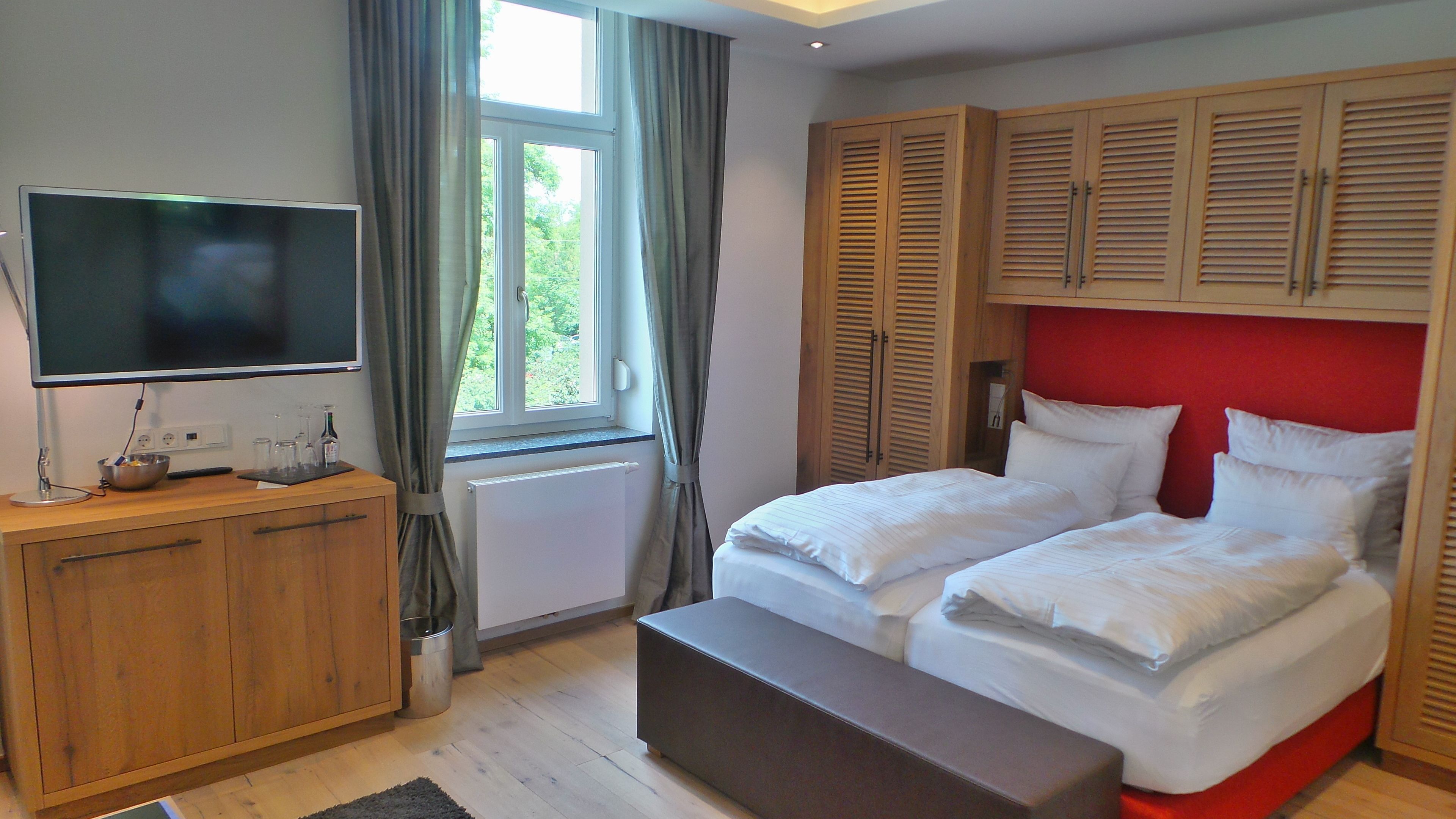 A bedroom with a bed, a TV, a wooden cabinet, and a window with curtains.