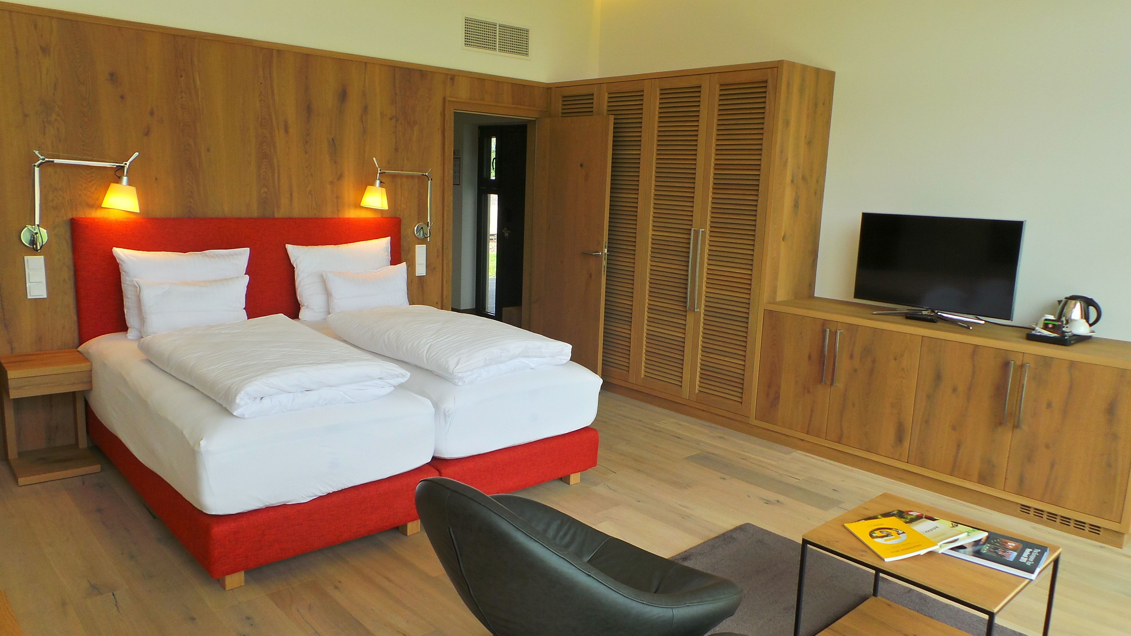 Habitación de hotel con cama doble, televisión, armario de madera y una mesita con libros.