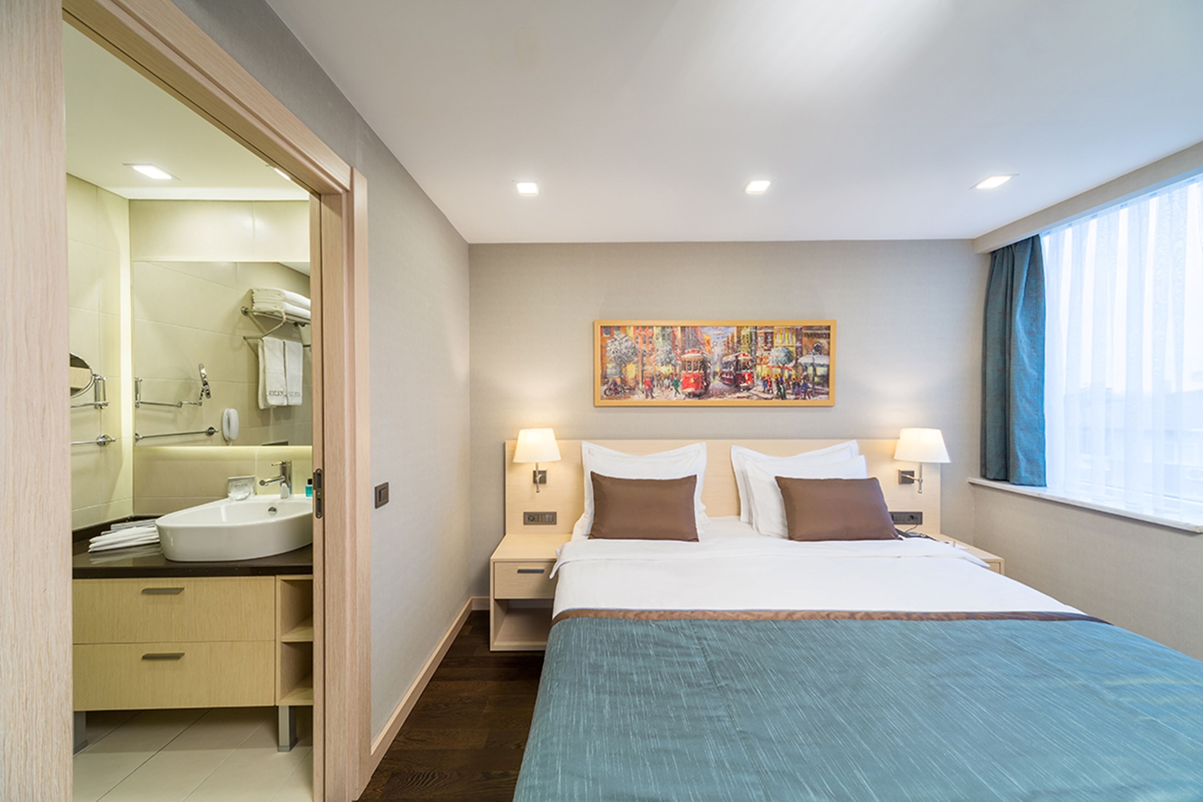 Ein Hotelzimmer mit Bett, einem Wandbild, einem Badezimmer mit Waschbecken und Spiegel sowie einem Fenster mit Vorhängen.