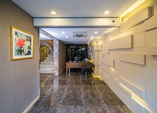 A modern hotel lobby with a marble floor, a staircase, a reception desk, and a framed artwork on the wall.