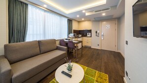 A modern hotel room with a sofa, a small dining table, a kitchen area, and a TV. -  Monapart Hotel Istanbul Mecidiyekoy (Istanbul)