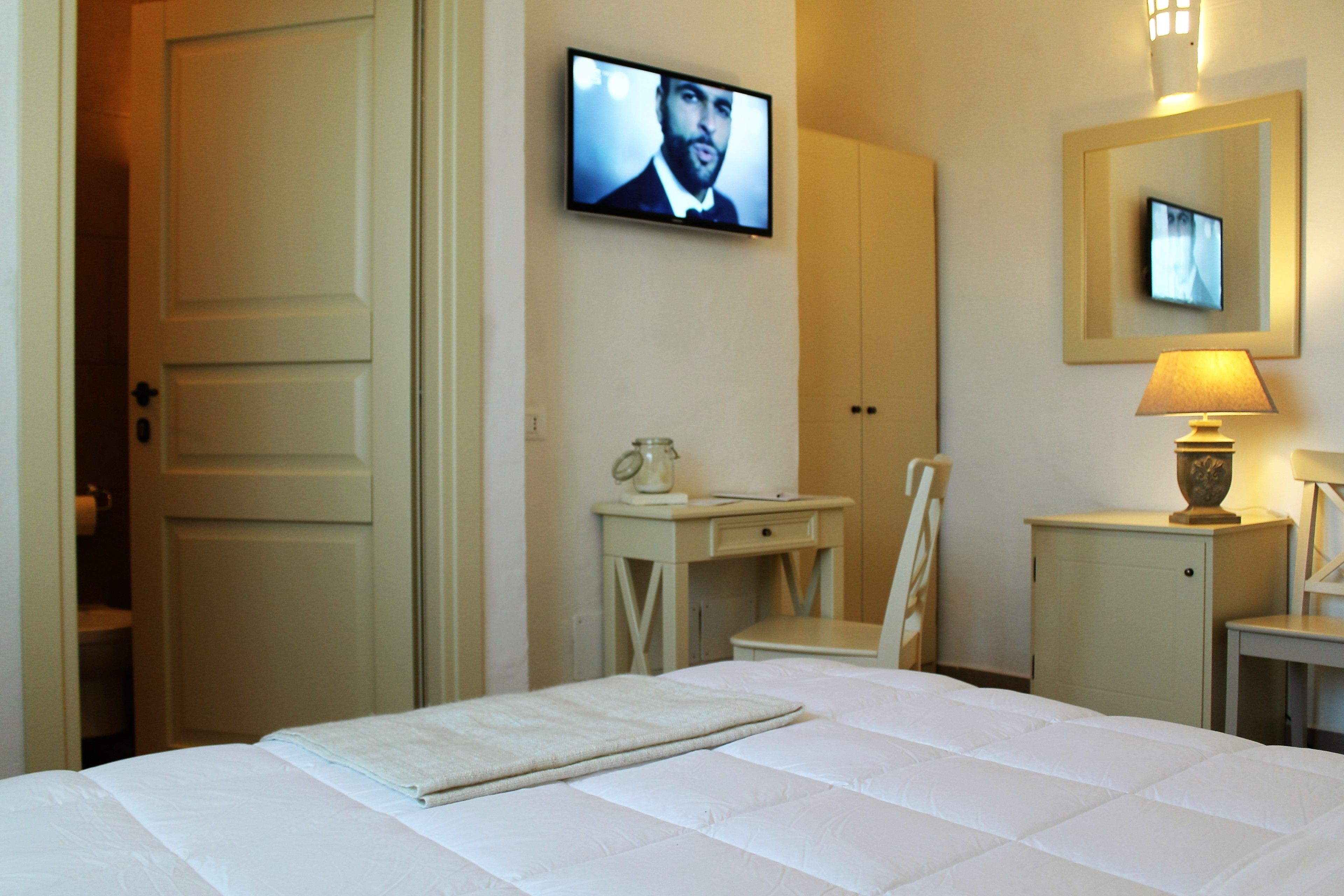 Habitación de hotel con cama, escritorio, silla, televisor y espejo.