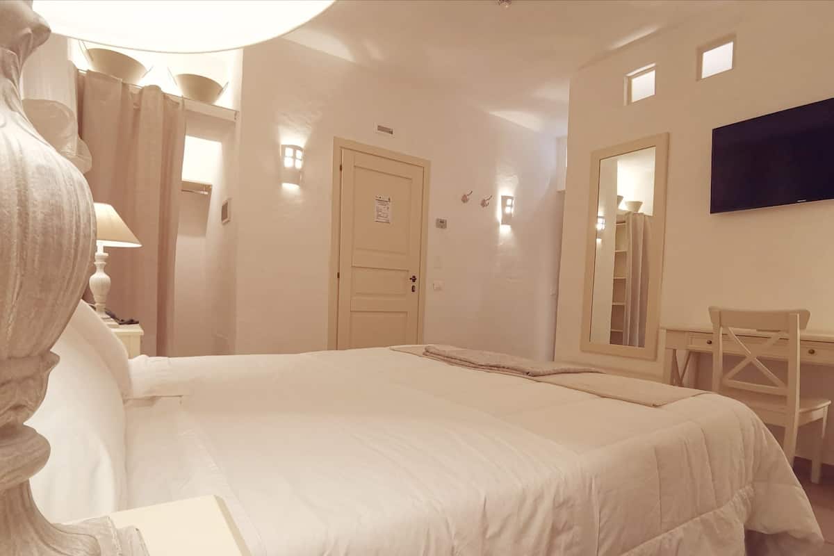 Ein Schlafzimmer mit einem großen Bett, einem Schreibtisch, einem Stuhl, einem Fernseher und einer Tür mit kleinem Fenster.