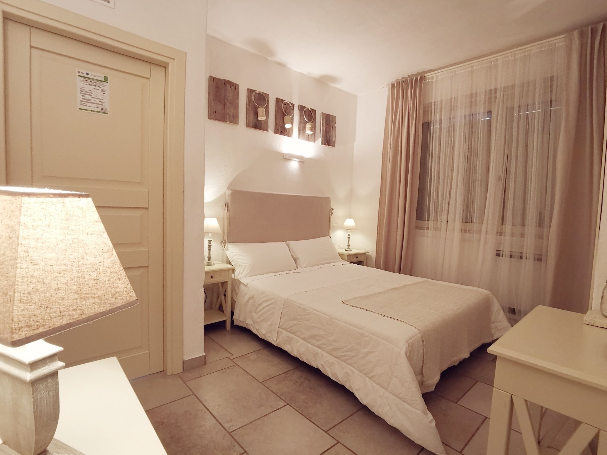 Een hotelkamer met een bed, twee nachtkastjes, een lamp, een spiegel en een raam met gordijnen.