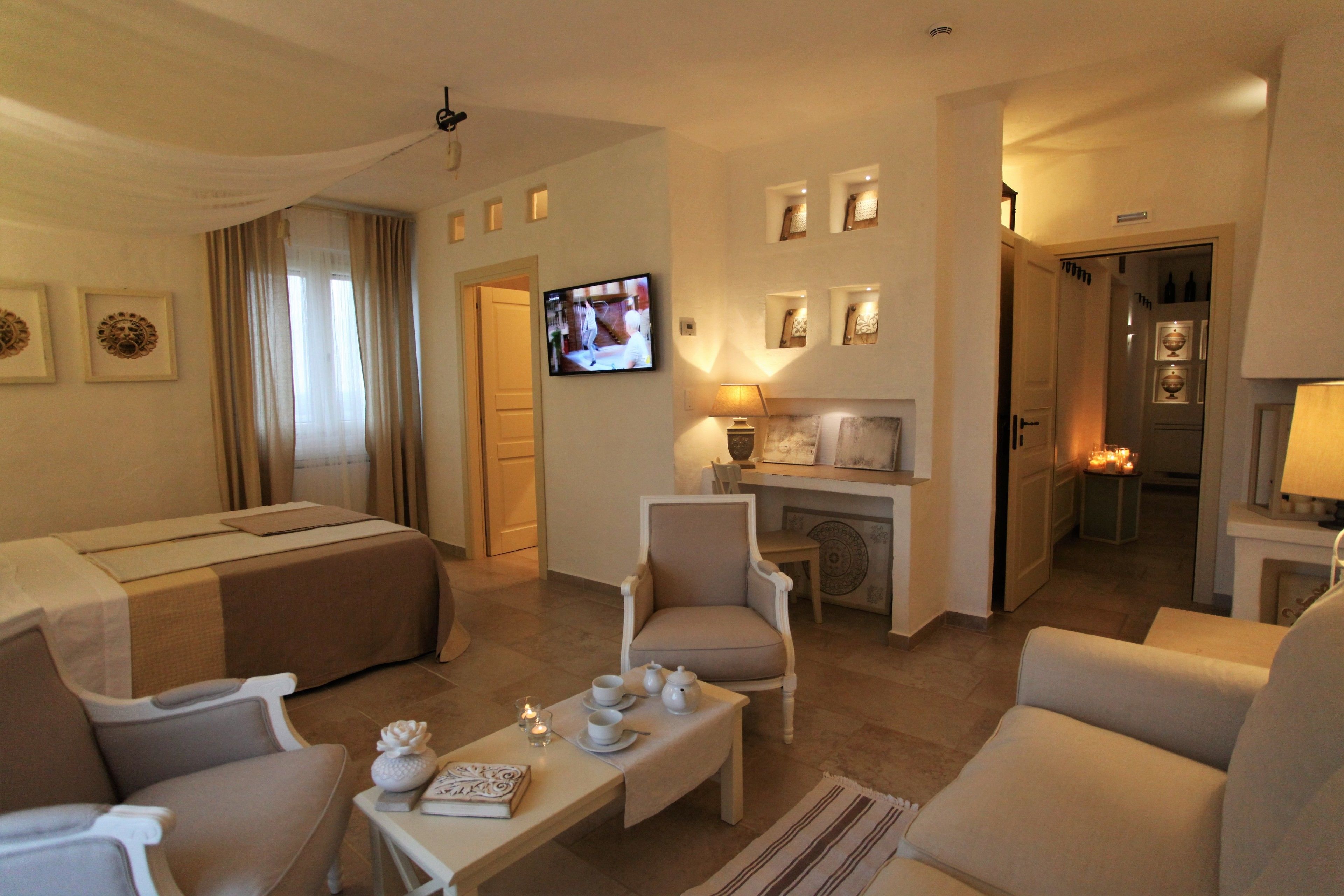 A hotel room with a bed, two armchairs, a coffee table, a television, and a fireplace.