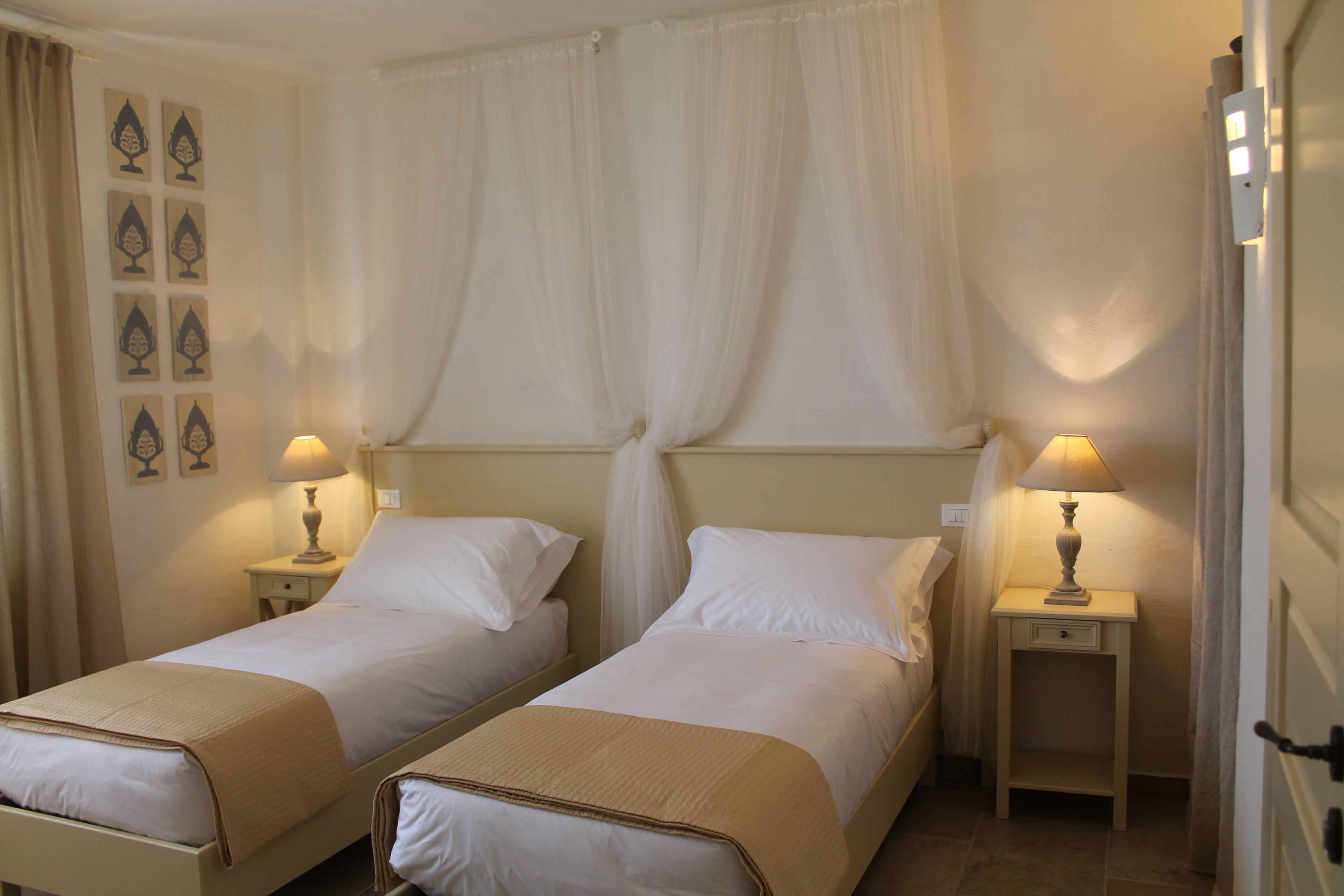 Ein Hotelzimmer mit zwei Betten, jeweils einem Nachttisch und einer Lampe, einem Vorhang und Wandbildern.