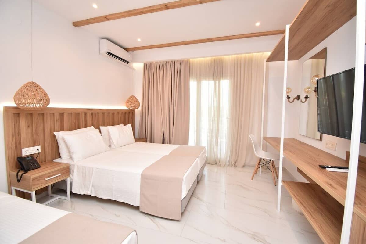 Una habitación de hotel moderna con cabecera de madera, cama con ropa blanca, escritorio con silla, televisor y una ventana grande con cortinas.